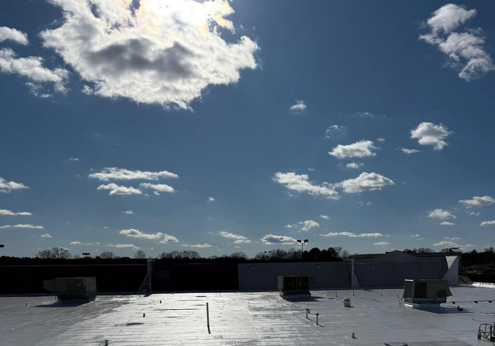 Reflective white waterproof roof coating on a commercial flat roof under a cloudy sky